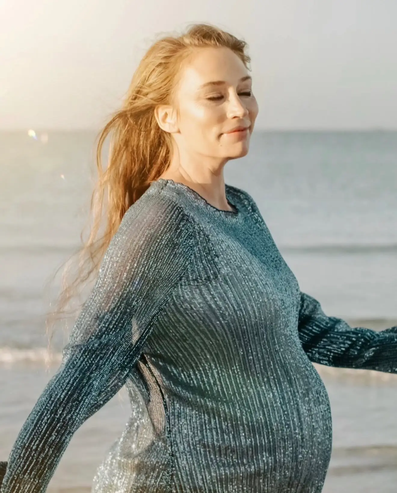 Séance grossesse au bord de l'eau : future maman souriante, cheveux au vent, dans la lumière du soir.