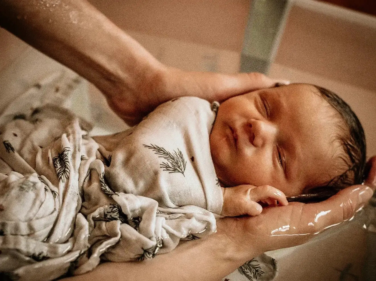 Séance naissance : premier bain du nouveau-né, porté par les mains de ses parents.