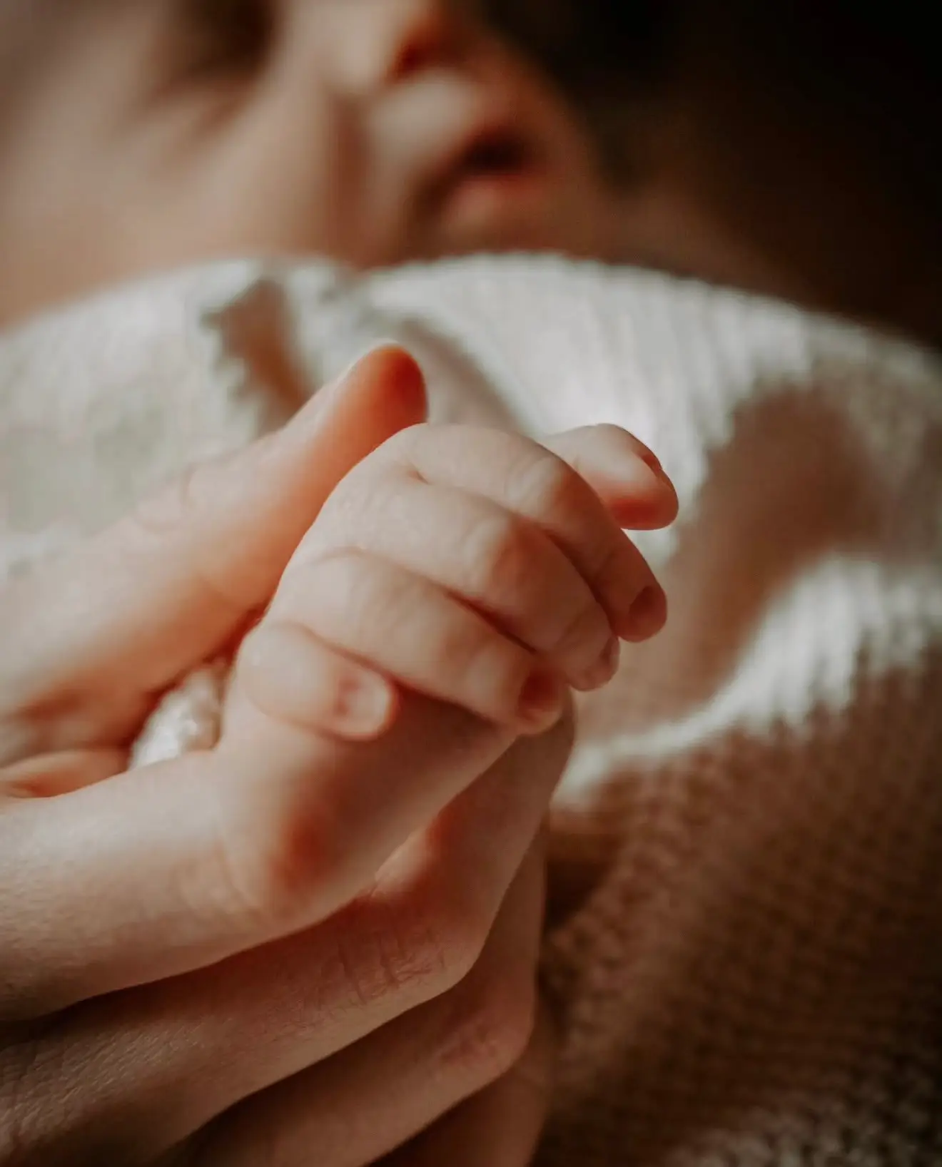 Séance naissance : la main du nouveau-né refermée sur les doigts de sa maman.