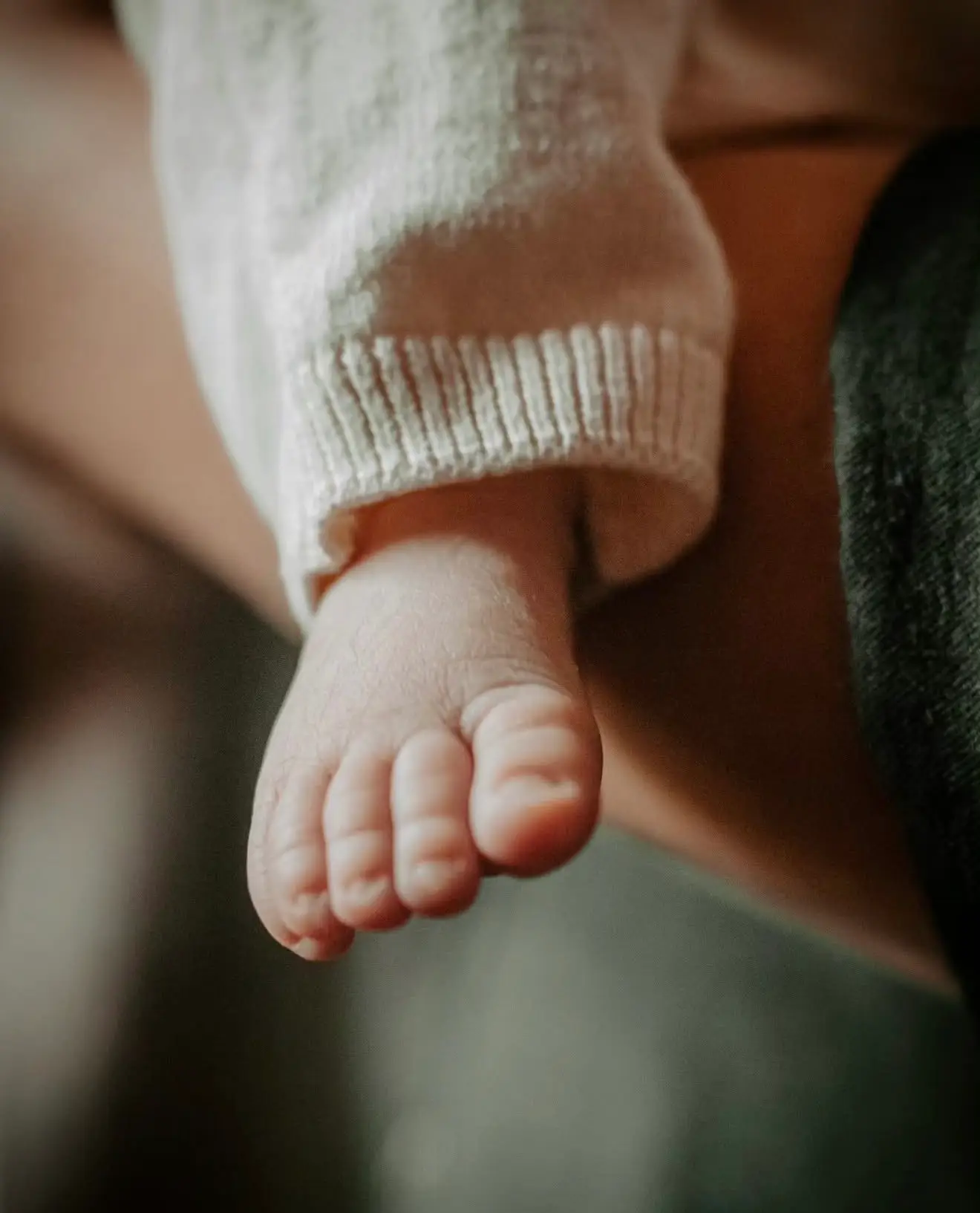 Séance naissance à domicile : détail des petits pieds du nouveau-né, blotti dans les bras de sa maman.