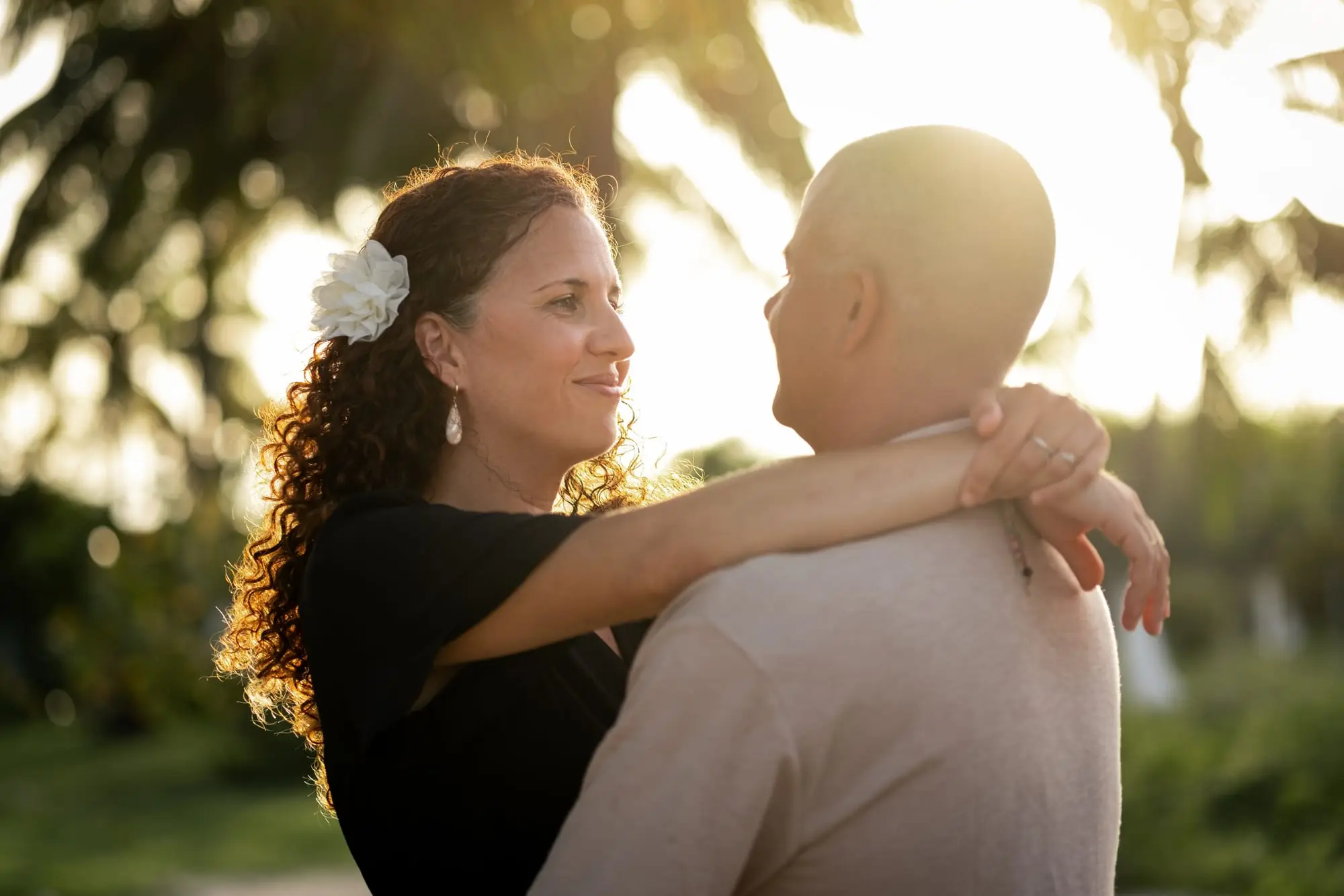 Séance couple sur la plage de Bois Jolan, à Sainte-Anne : une femme, une fleur blanche dans les cheveux, enlace son compagnon face au soleil couchant.