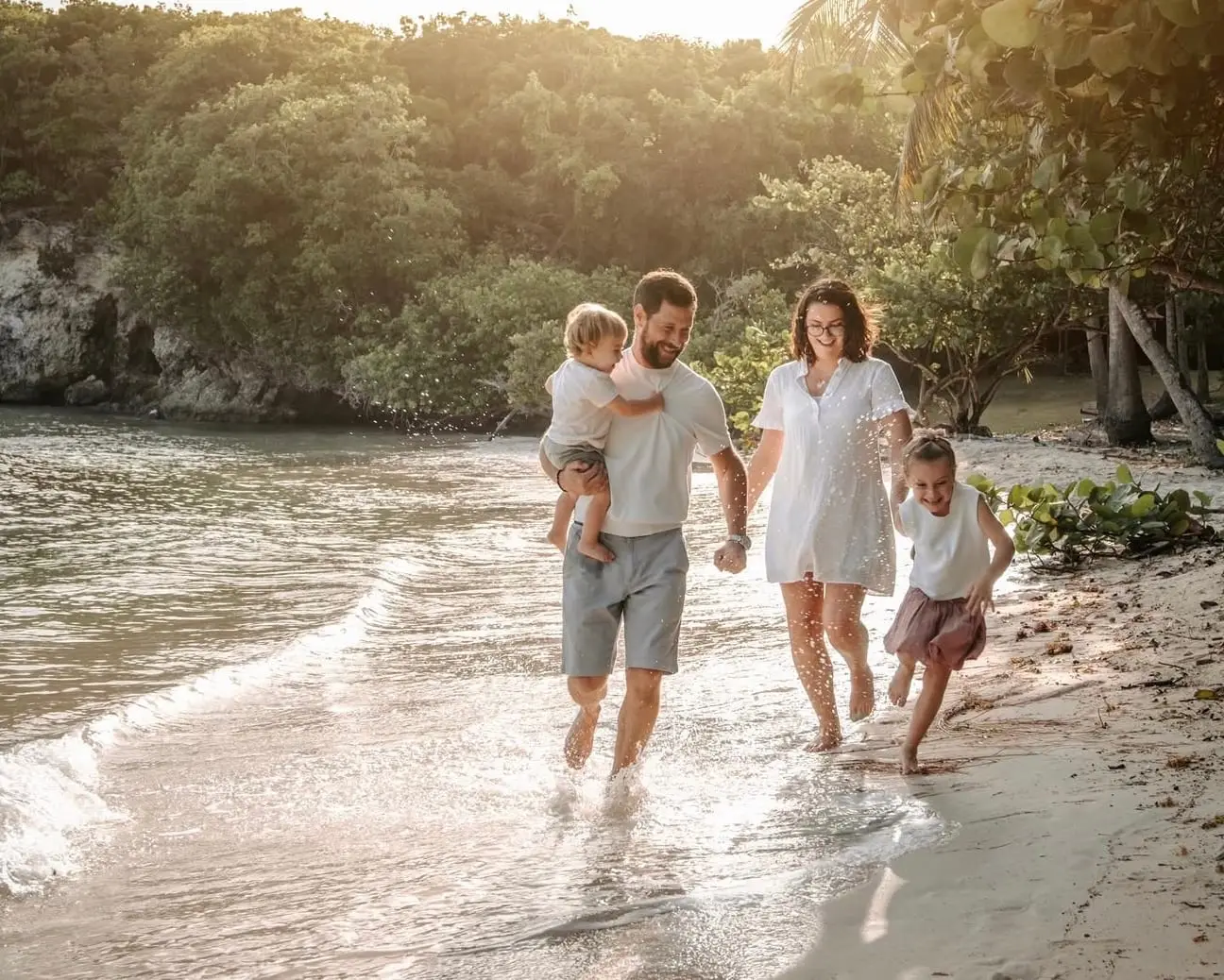 Séance famille au bord de l'eau, à l'Anse à Jacques : les parents et leurs deux enfants courent dans les vagues au coucher du soleil.