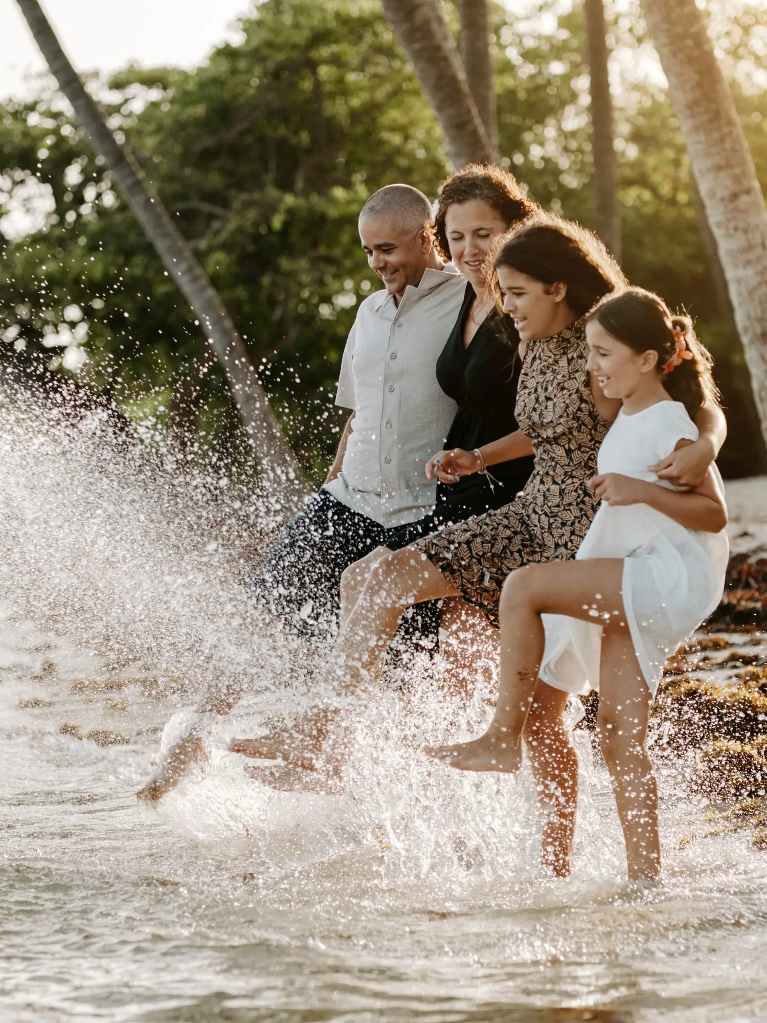 Séance famille sur la plage de Bois Jolan, à Sainte-Anne : les parents et leurs deux filles shootent l'eau du pied dans une grande gerbe d'éclaboussures.