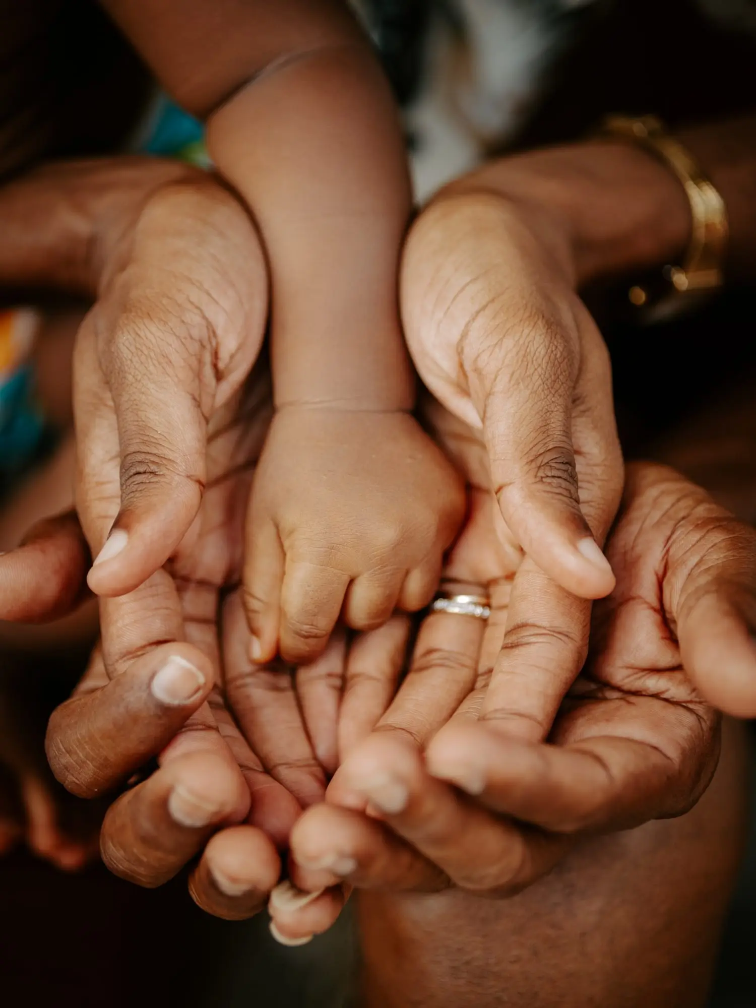 Séance naissance à Sainte-Anne : les mains de trois générations réunies en coupe autour des petites mains du bébé.