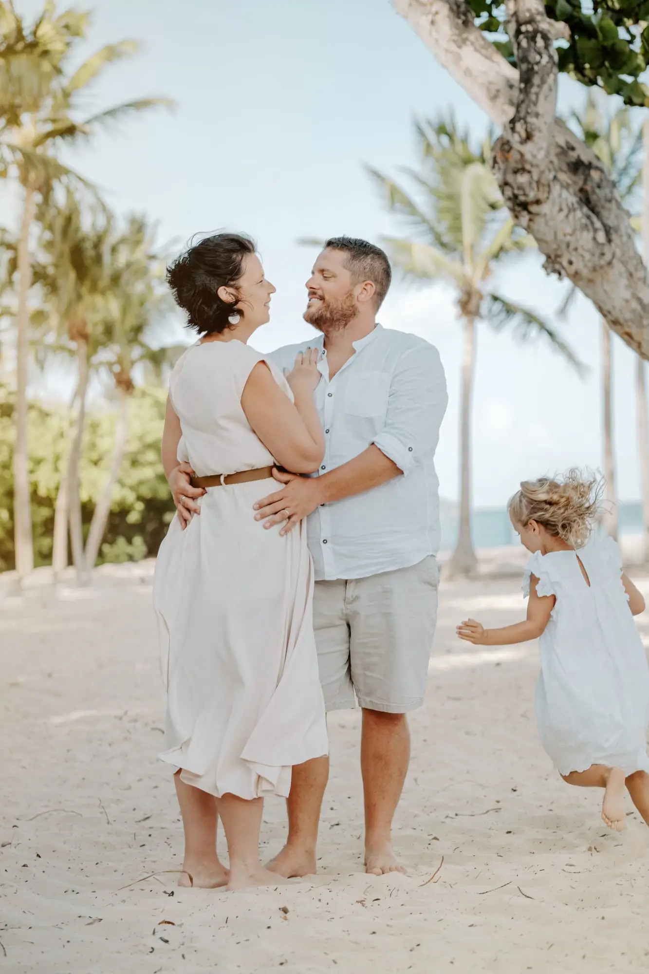 Séance de vacances sur la plage de Bois Jolan, à Sainte-Anne : les parents enlacés sous les cocotiers, leur fille qui court vers eux.