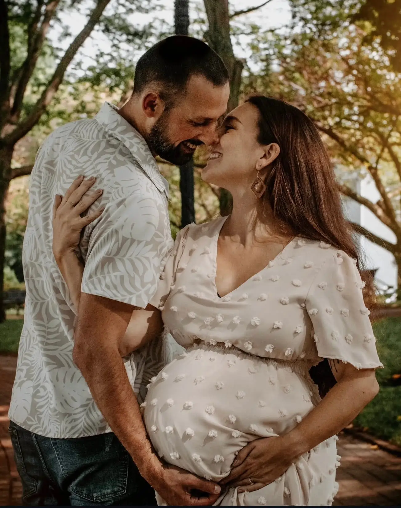 Séance grossesse en couple : les futurs parents nez à nez en riant, leurs quatre mains réunies sur le ventre.