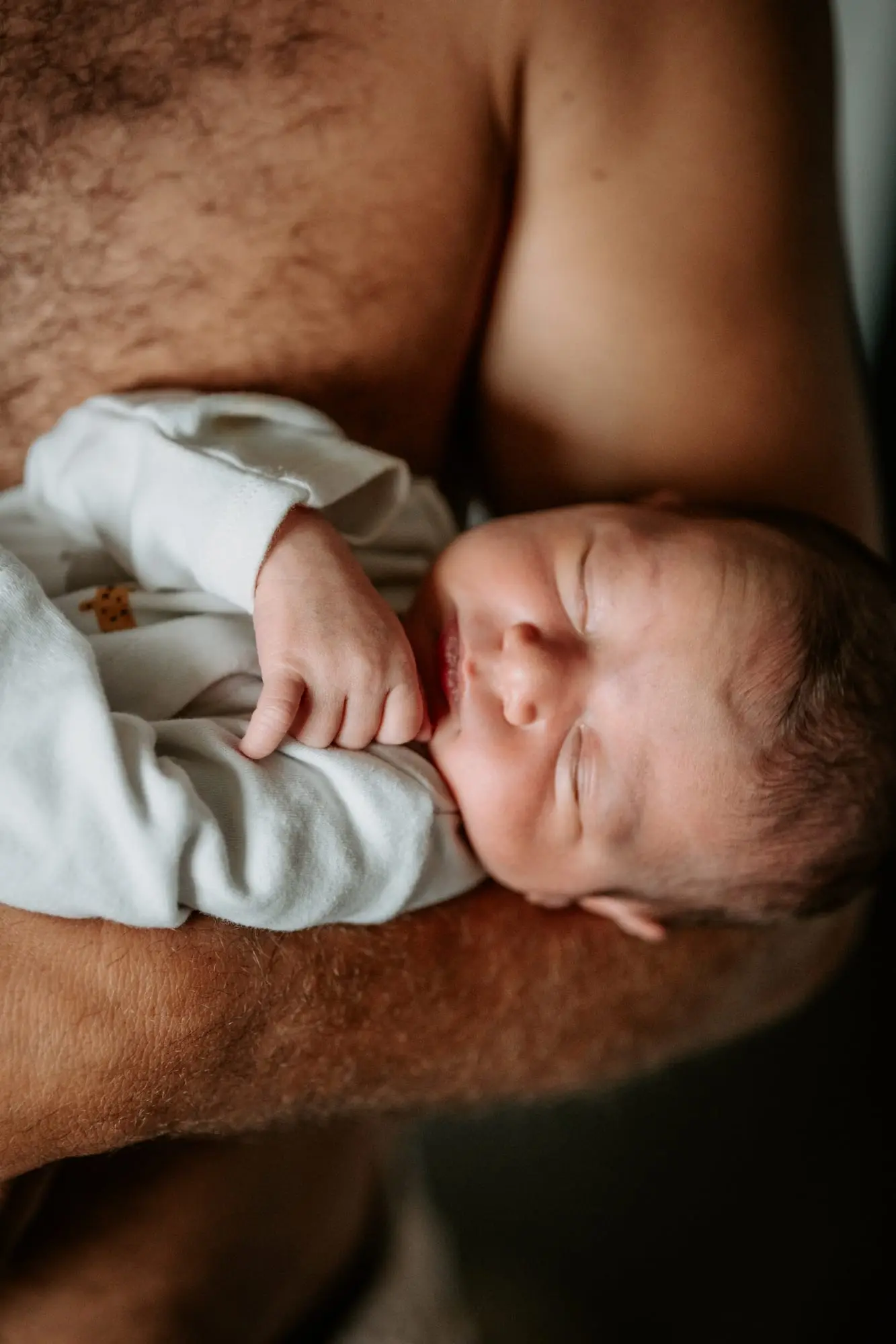 Séance naissance à domicile, à Sainte-Anne : nouveau-né endormi en peau à peau contre le torse de son papa.