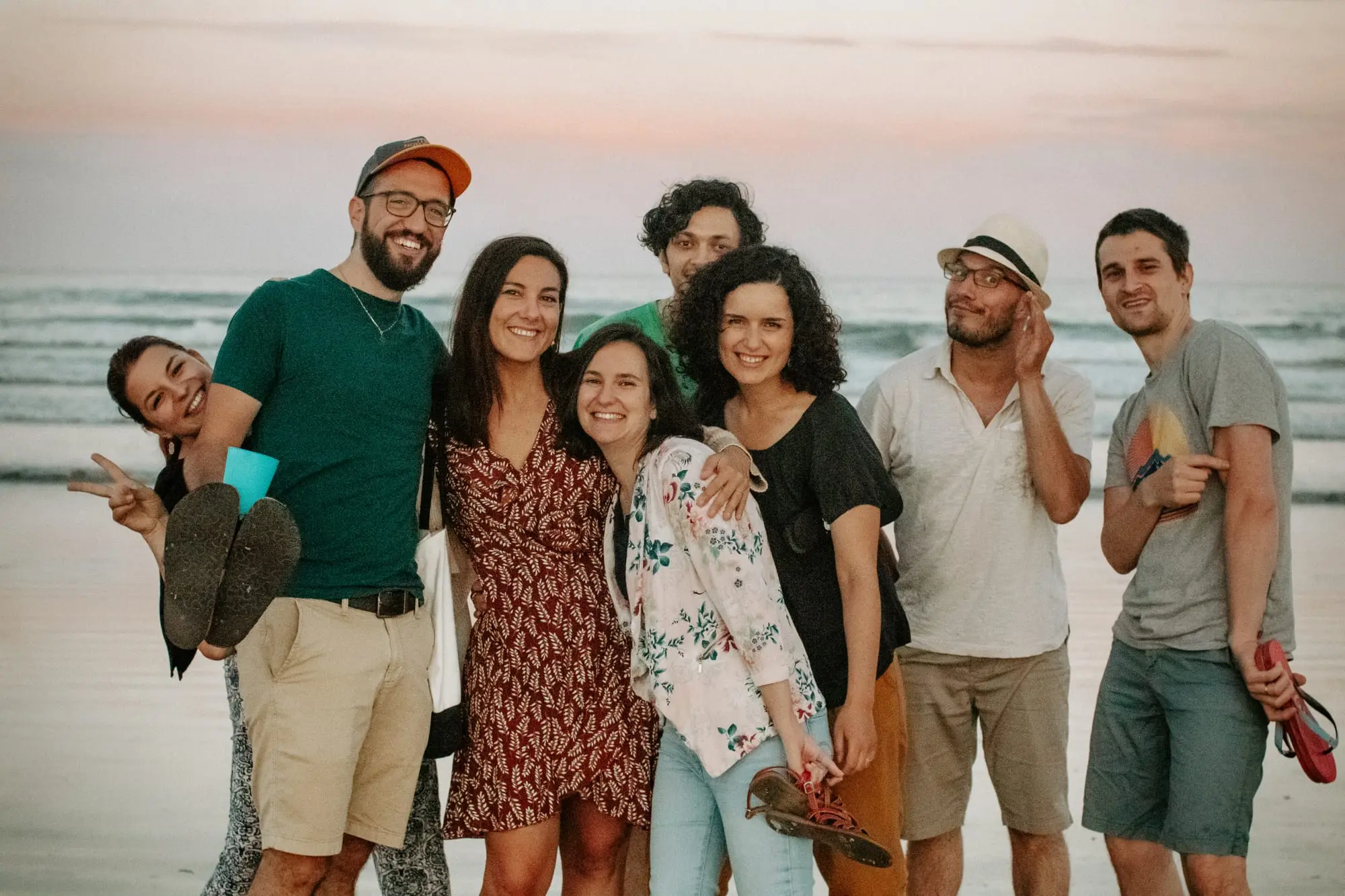 Séance entre amis sur la plage : les huit copains serrés épaule contre épaule face à l'objectif, dans le ciel rose de fin de journée.